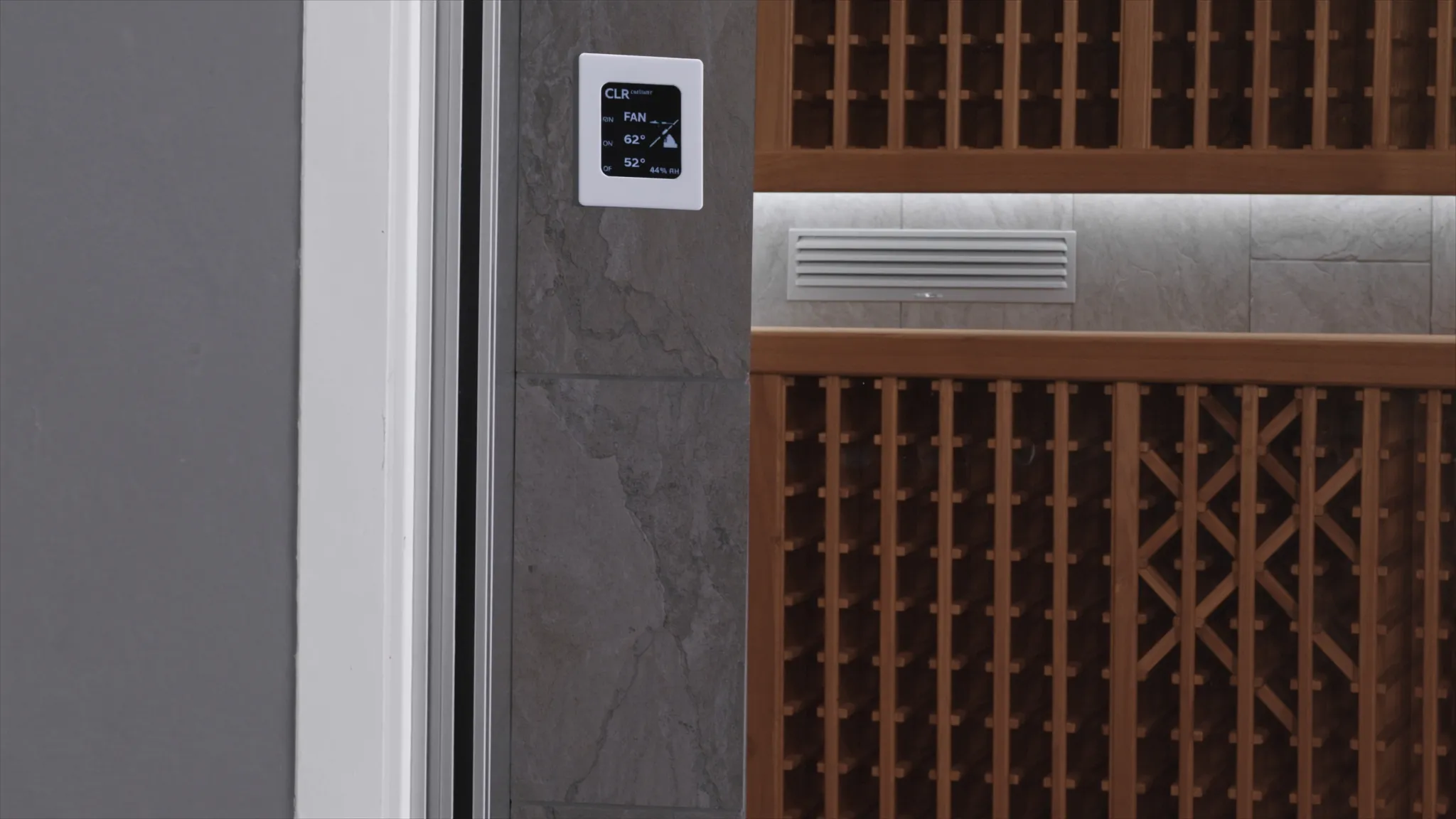 Wine cellar control panel and supply grille beside bottle racks, showing the building details behind stable cellar temperature